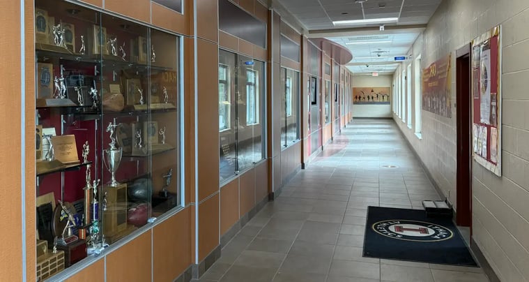School hallway featuring a large glass trophy case filled with athletic awards, trophies, plaques, and sports memorabilia.