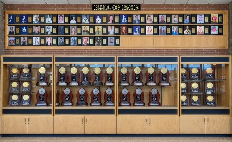 Straight-on view of Thompson Valley High School’s Athletics Legacy Hall, featuring a black brick wall with gold-and-white school branding, championship achievements, an eagle logo, commemorative plaques, and a centrally mounted interactive touchscreen display.
