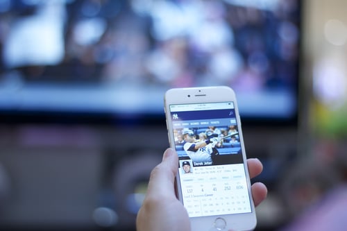 Sports fan looking at Derek Jeter statistics on iPhone while watching baseball game